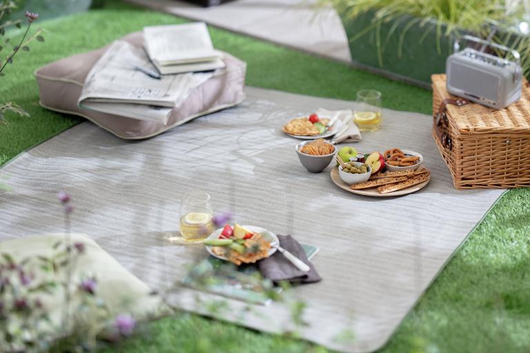Grey picnic blanket and picnic set up on grass.