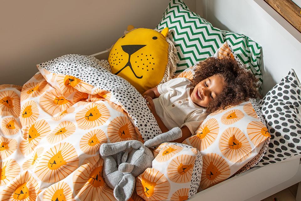 Image of a kid in bed surrounded by lots of colourful duvets and pillows.