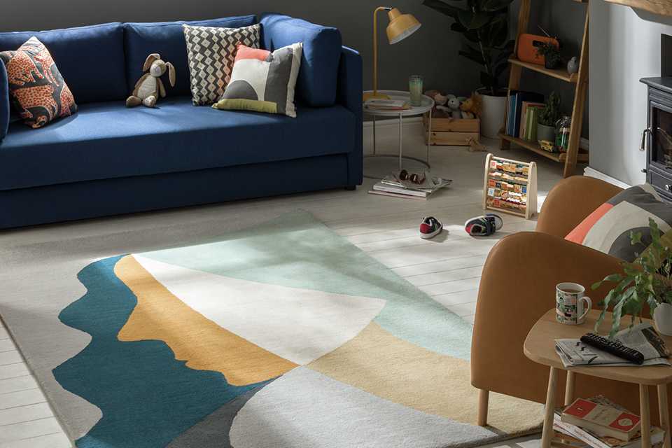 An abstract pastel coloured rug on a white wooden floor beside a navy blue sofa.