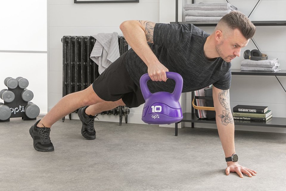 A man performing a kettlebell exercise using a purple kettlebell in a room.