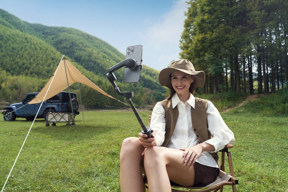 A woman using a DJI Osmo Mobile 6 handheld camera for a self portrait while camping. 