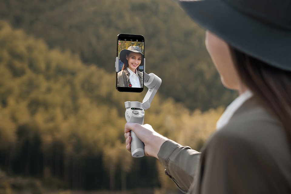 A woman taking a self portrait in the forest with the DJI Osmo Mobile SE. 