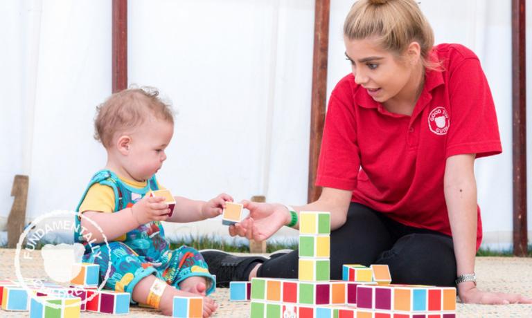 A baby plays with coloured blocks with the help of a young woman.