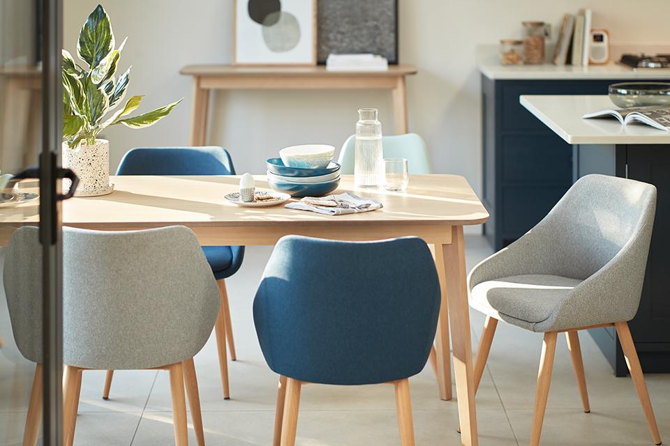 Image of a pine dining table surrounded by grey and blue scandi-style chairs.