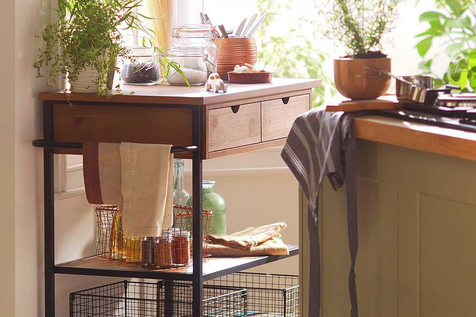 Wooden kitchen trolley in kitchen with wired baskets on trolleys shelf.