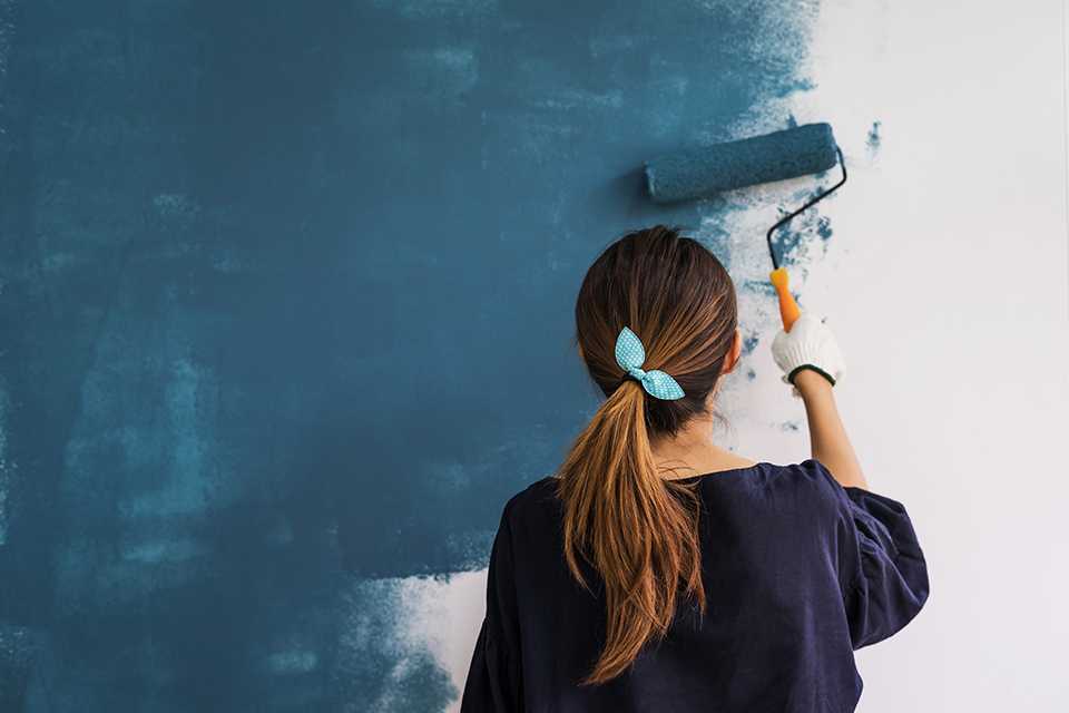 A woman paints a wall with a paint roller.