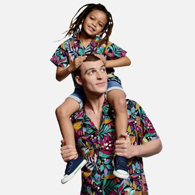 A father and child in matching Hawaiin shirts. The child is sitting on her father's shoulders.