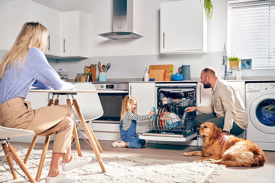A family putting the dishes inside a built-in Indesit dishwasher in the kitchen. 