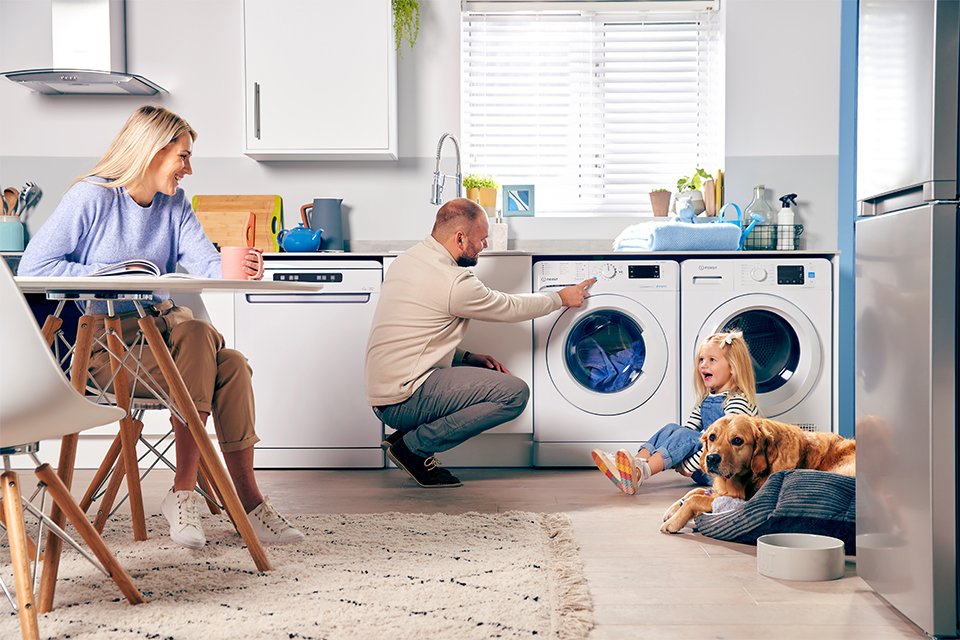  A man operating an Indesit washing machine while surrounded by his family in a living room setup.