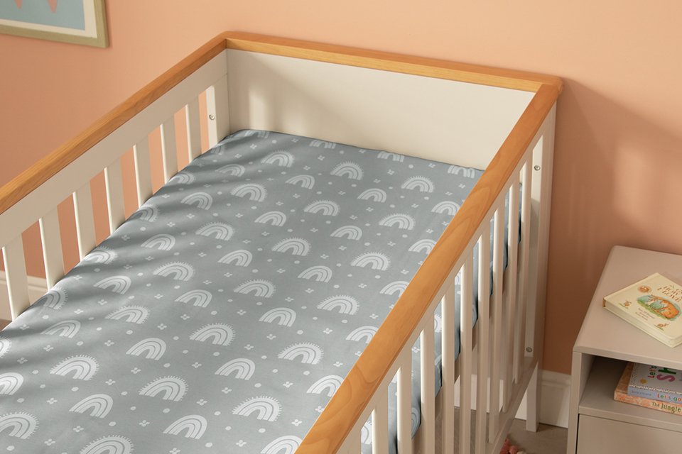 A Habitat rainbow themed grey fitted sheet on a cror mattress.