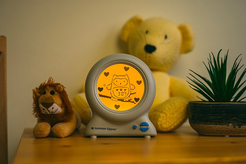 A Tommee Tippee Groclock 3-in-1 sleep trainer, alarm clock and nightlight on a table.
