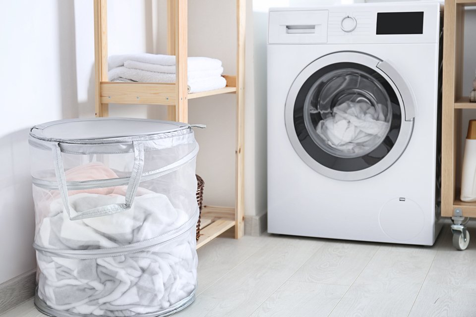 A white washing machine in a utility room next to a wooden storage rack and white laundry basket. 