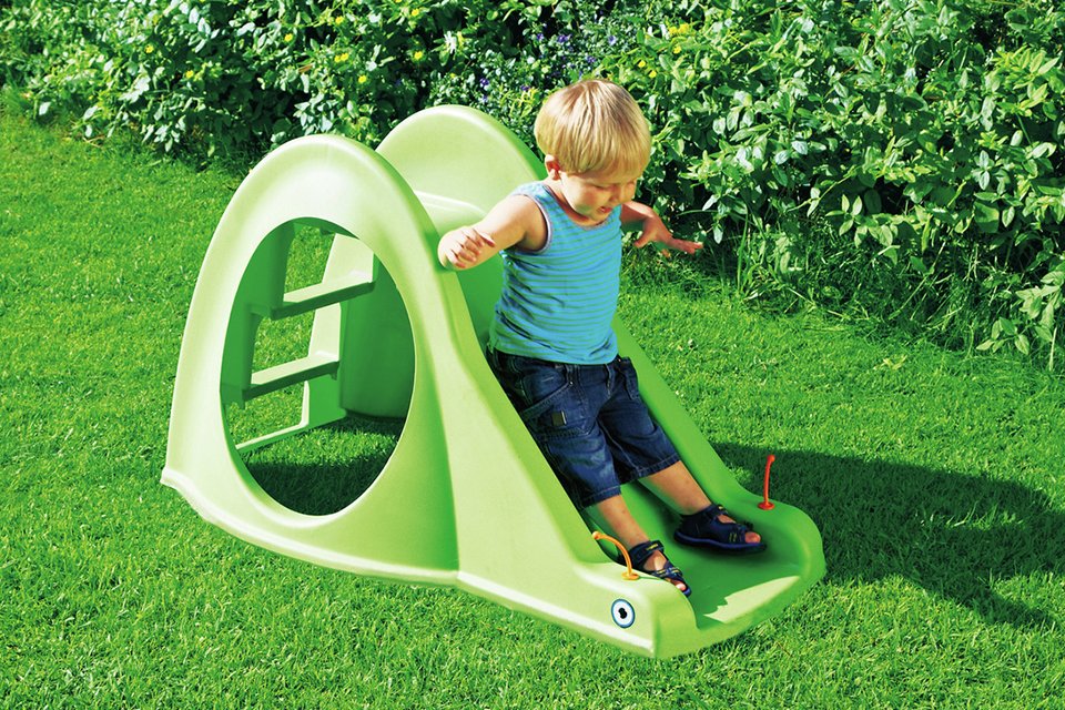 A small boy playing on a green slide in the garden.