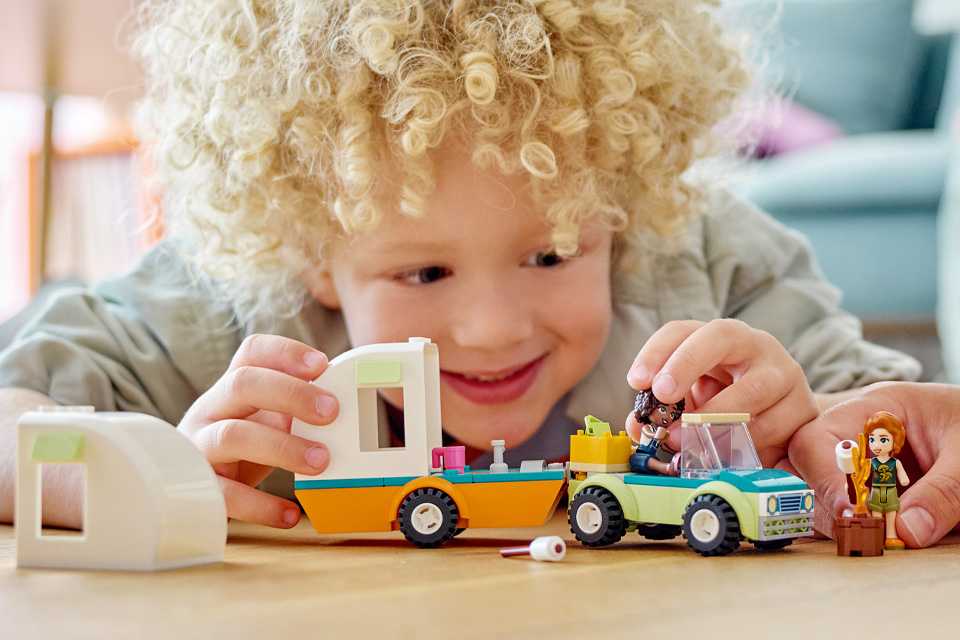A young boy playing with a LEGO® Friends Holiday Camping Trip Camper Van toy set.