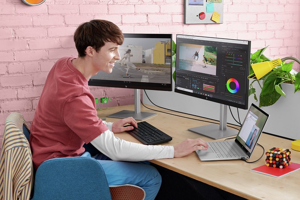 A boy working on two desktops and a laptop sitting on a table in front of him.