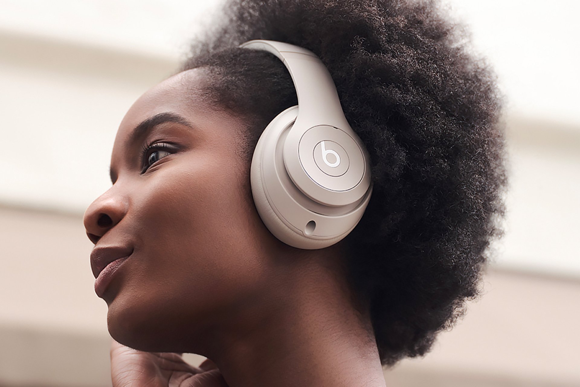 A woman wearing Beats Studio Pro headphones in Sandstone colour.
