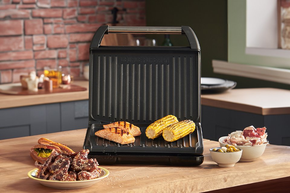 An open George Foreman health grill with fish and corn grilling on it. 