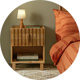 Wooden ribbed side drawers next to bed with orange bedding in green room.