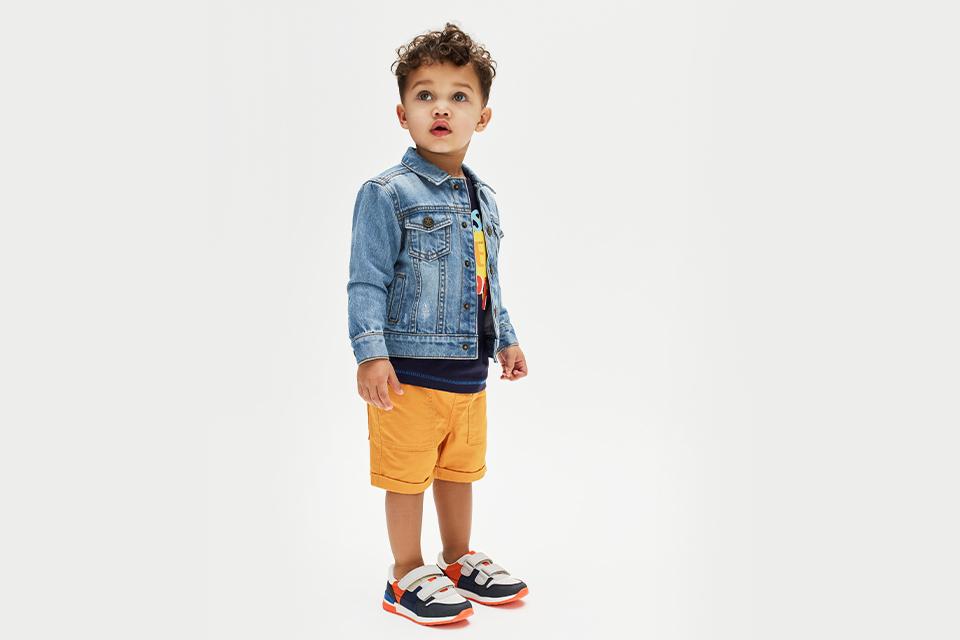 Young boy in yellow shorts and blue denim jacket.