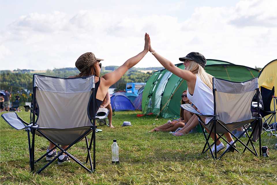 Two young women giving each other a high five in a camp.