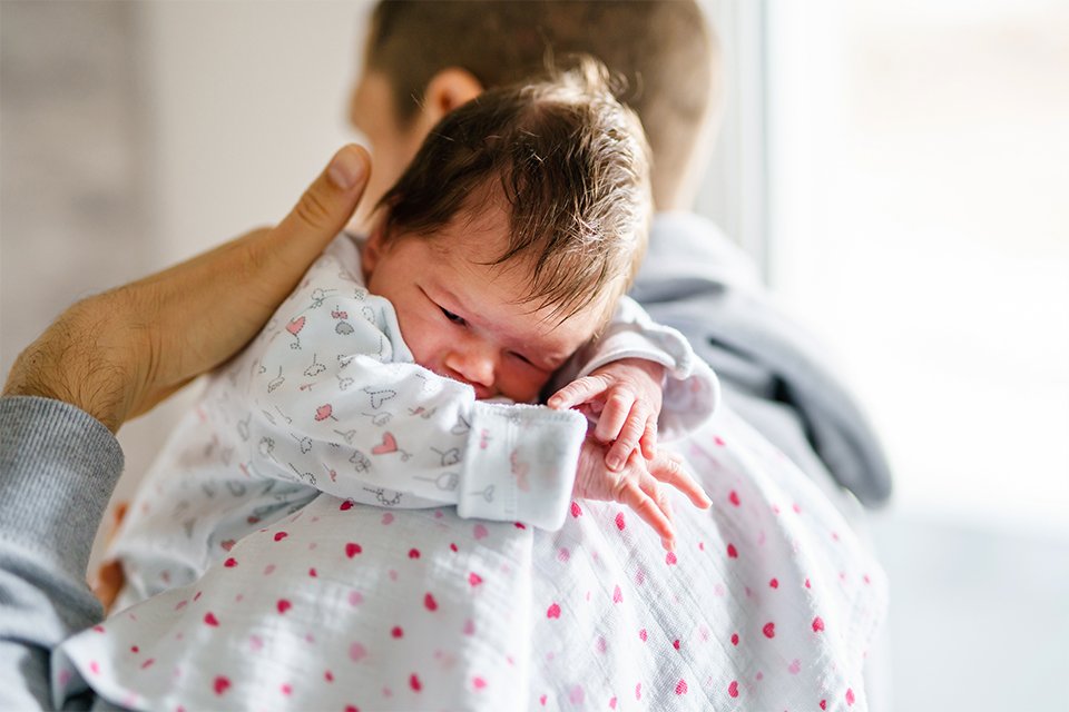 A baby's head resting on a muslin square on the father's shoulder.