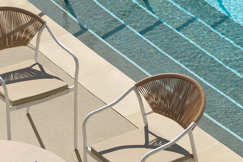 Habitat wooden effect garden chairs placed next to a table with white Habitat plates and cutlery near a swimming pool.