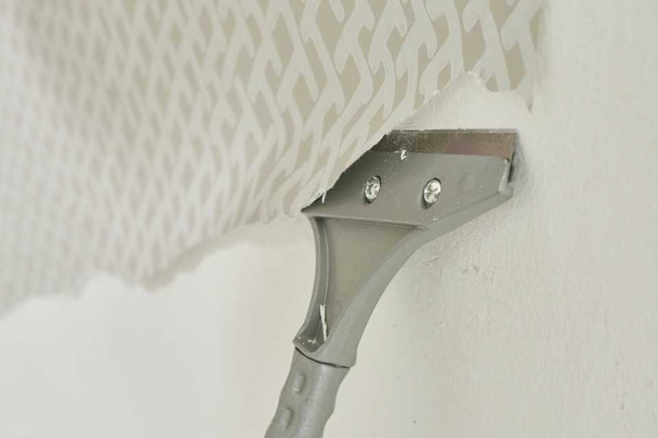 A metal scraper scraping wallpaper off a wall.