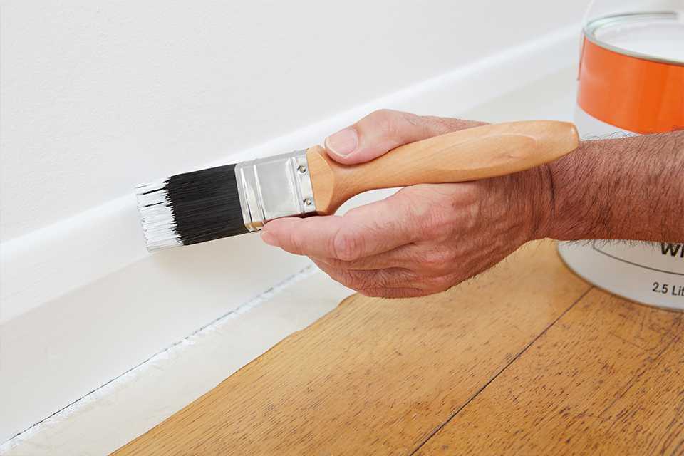 Person painting white gloss onto a skirting board.
