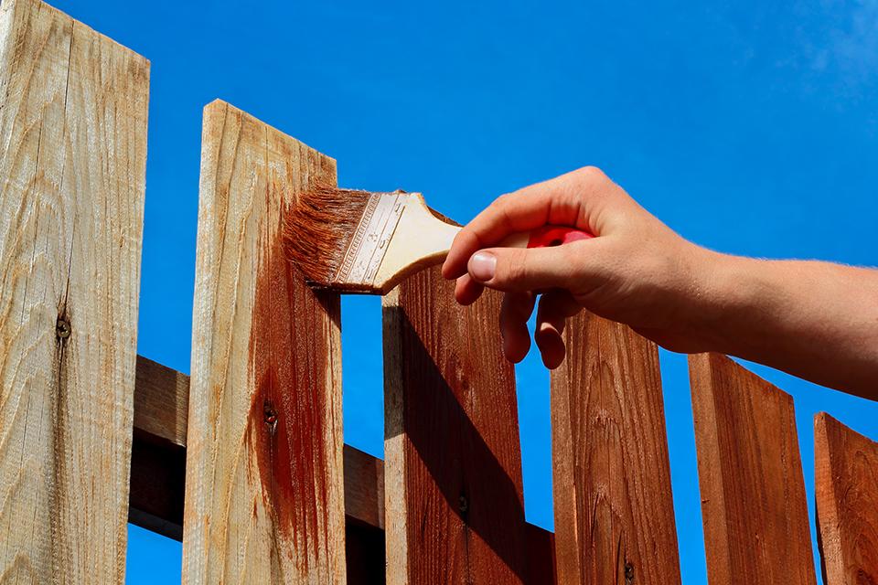Person painting a fence brown.