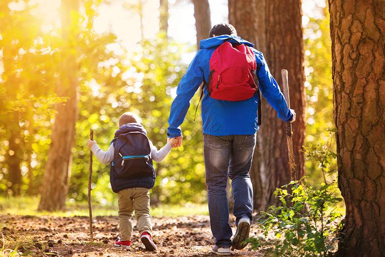 Father and son walking in forest with rucksacks.