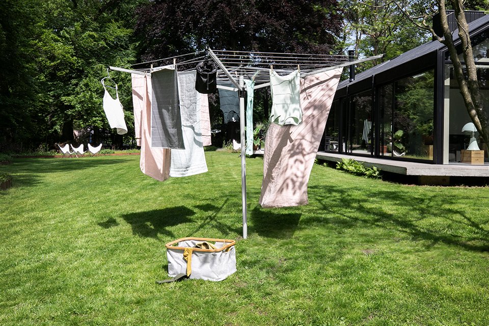 Clothes hanging on a Brabantia washing line outside a house with a laundry basket next to it.