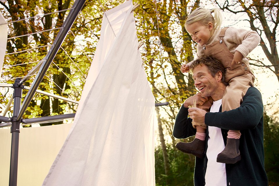 A man carrying a young girl on his shoulders next to a Brabantia washing line.