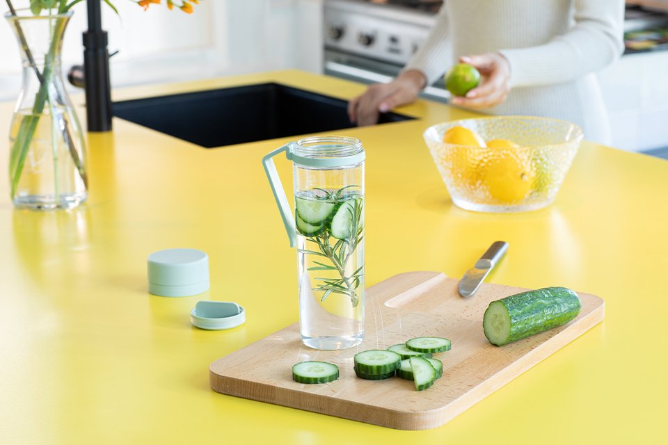 A Brabantia water bottle placed on a chopping board next to a chopped cucumber and a knife.