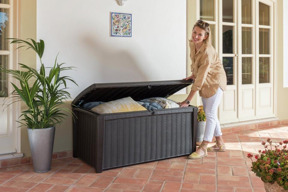 A woman storing cushions in a brown rattan effect garden storage box. 