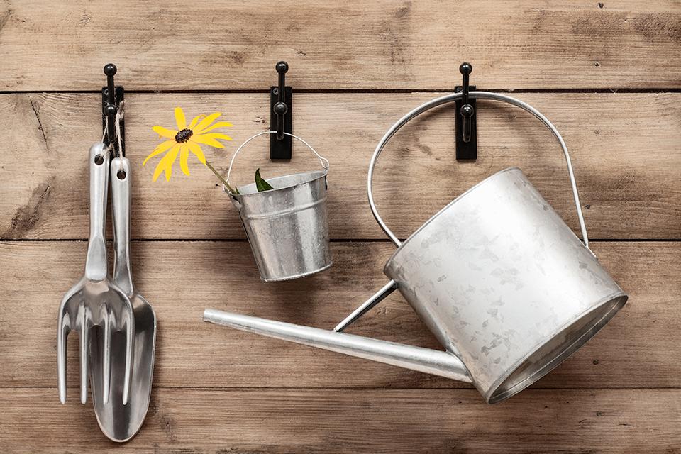 A metal watering can and gardening hand tools, hung up on hooks.