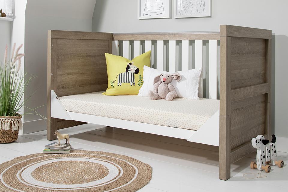 The Modena baby cot bed in white and oak with one side of the cot removed.
