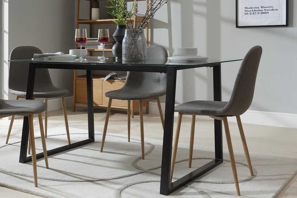 A glass-topped dining table with black legs and grey upholstered chairs.
