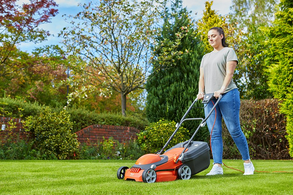 A woman mowing a lawn using a Flymo® EasiStore 340R electric lawnmower. 