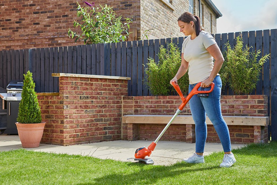 A woman using a Flymo® EasiTrim grass trimmer to trim a lawn. 