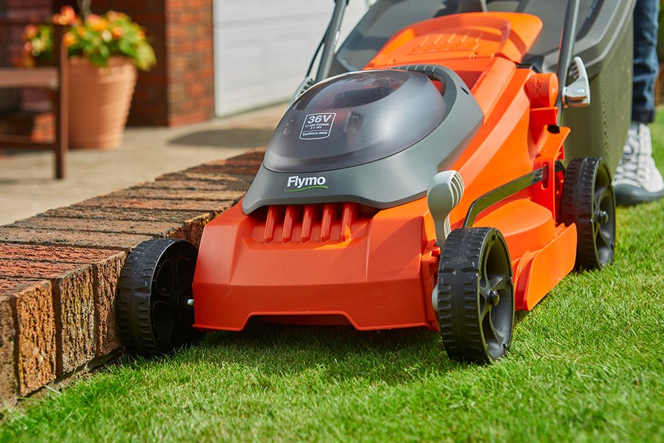 A person using a Flymo® SimpliStore cordlesss rotary lawnmower to mow a lawn. 
