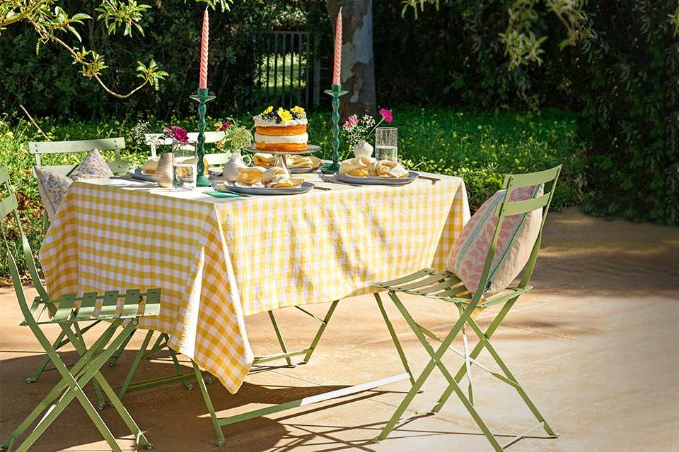Green metal garden table and chairs with yellow gingham tablecoth.