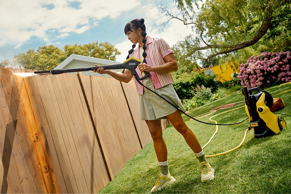 A woman using a Kärcher pressure washer to clean a fence in her garden.