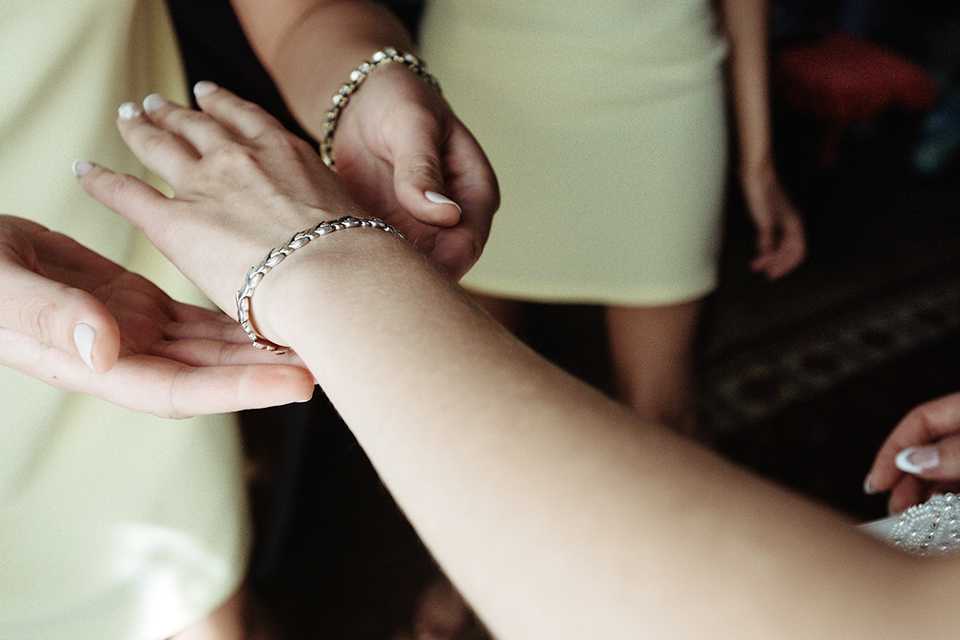 A woman putting on a silver bracelet on another woman's wrist.