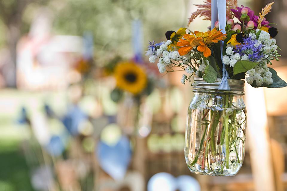 A jam jar containing flowers hanging from the tree.