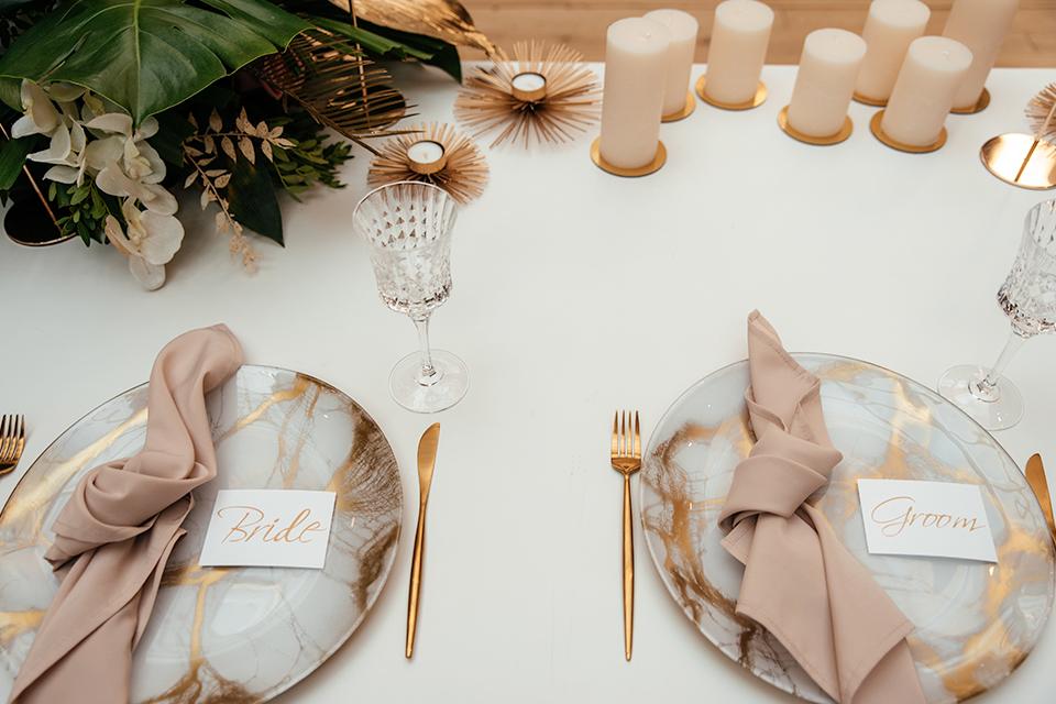 A dinner table setting for bride and groom with metallic and pastel accessories.