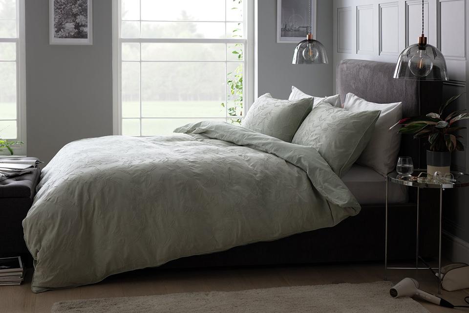 A grey velvet bed with sage green jacquard bedding in a grey boutique style bedroom.