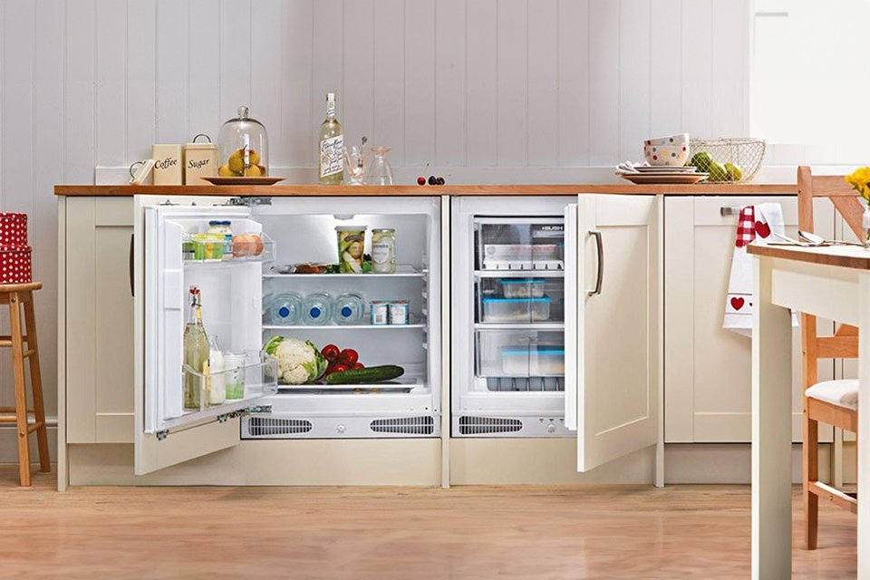 A Bush integrated under counter white freezer filled with water and veggies.