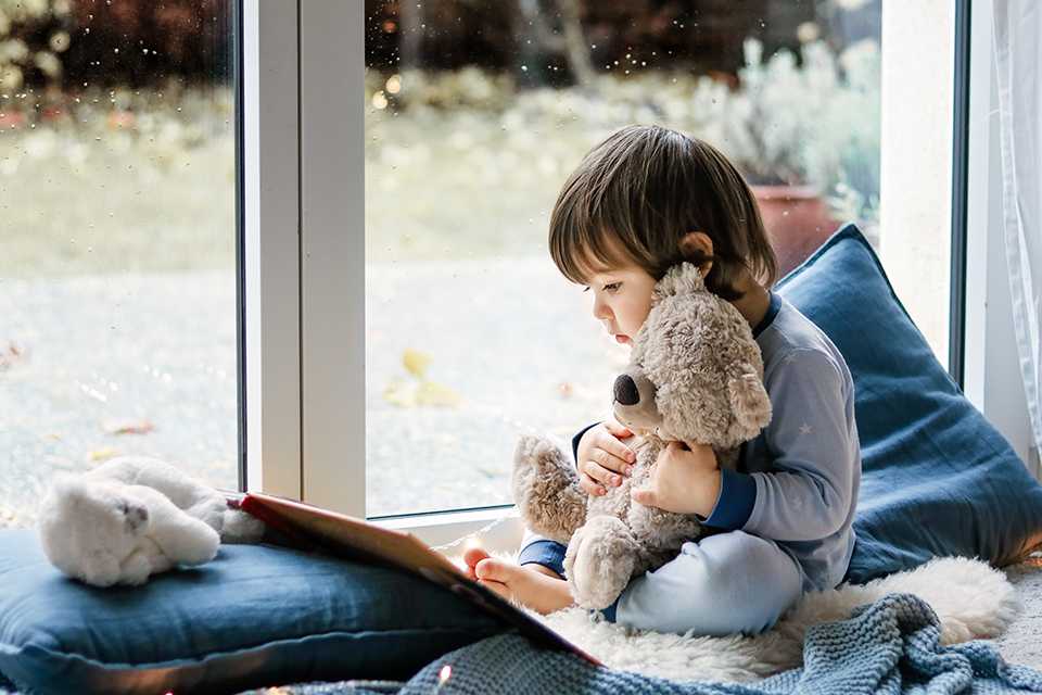 A toddler holding a teddy bear and exploring a story book.