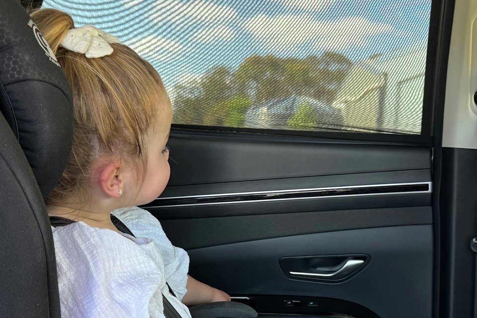 A girl looking out through a Dreambaby Car Window Shade/Socks.