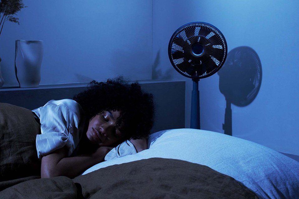 12 inch Duux Whisper Grey Pedestal Fan placed in a bedroom.